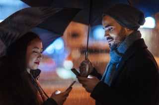 casal olhando pro celular e segurando guarda-chuva