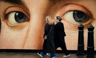 Pessoas caminhando em frente a um painel com olhos ilustrados