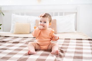 Bebê menina sentada na cama com roupa e laço na cabeça coral