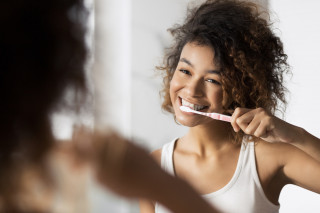 Mulher escovando os dentes enquanto se olha no espelho