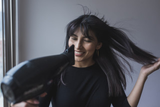 Mulher sorrindo com um secador de cabelo na mão direita
