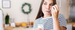mulher comendo um pote de iogurte na cozinha