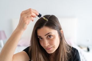 Mulher aplicando produto em conta gotas na raiz do cabelo