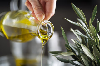 Imagem aproximada de pessoa despejando azeite de oliva de uma pequena jarra de vidro