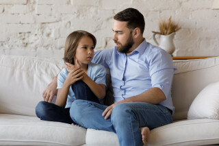 Pai sério conversando com filho/criança, ambos sentados em um sofá