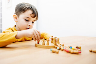 Menininho brincando com um jogo de tabuleiro de madeira em terapia educacional