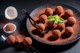 Trufas de chocolate em um prato com folha de hortelã no meio, ao redor, colheres e forminhas de papel