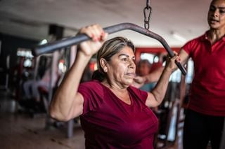 Senhora madura fazendo exercício na academia com ajuda de uma personal trainer