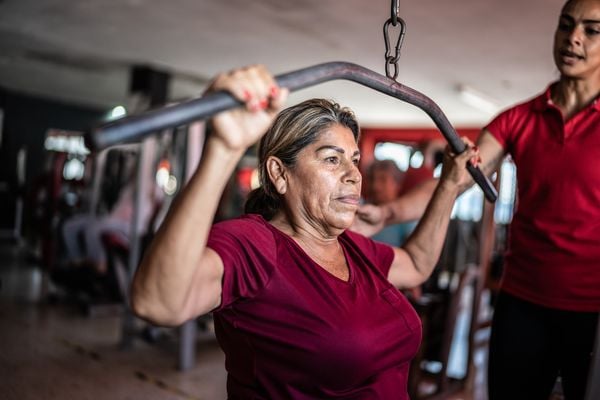 Senhora madura fazendo exercício na academia com ajuda de uma personal trainer