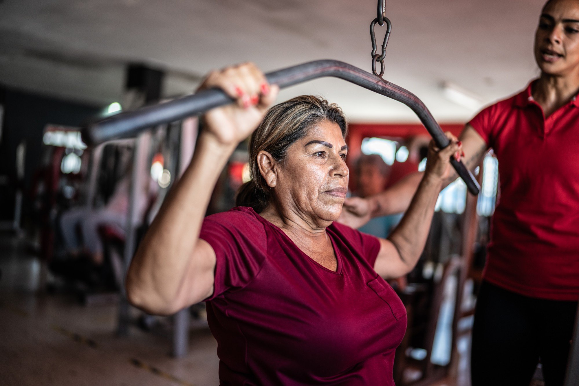 Senhora madura fazendo exercício na academia com ajuda de uma personal trainer