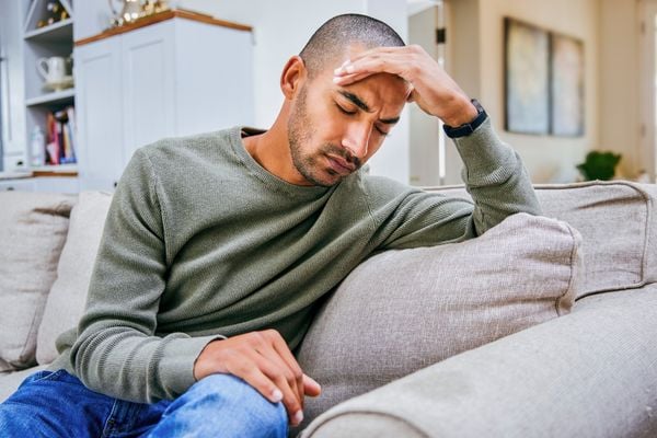 Homem sentado em um sofá com a mão na cabeça sentindo dor