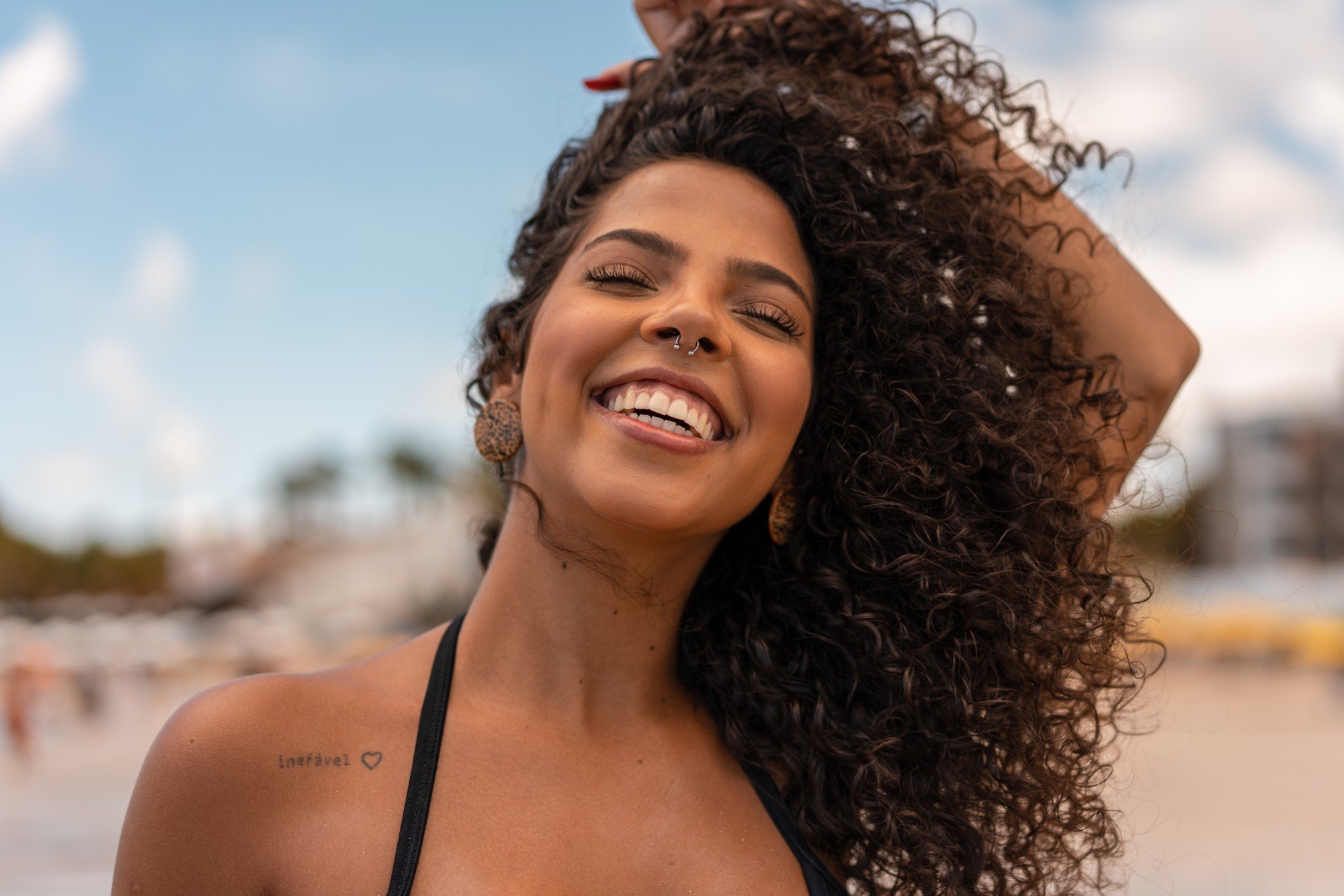 Mulher de cabelos cacheados sorrindo na praia