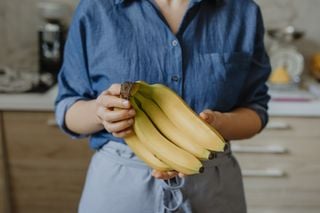 Imagem aproximada de mulher segurando cacho de banana