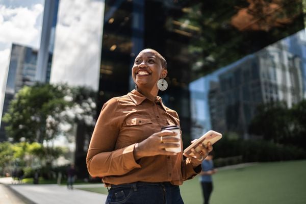 Mulher olhando para o céu enquanto segura um celular e um copo de café