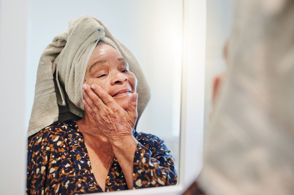 Mulher sorrindo com toalha na cabeça e creme na bochecha