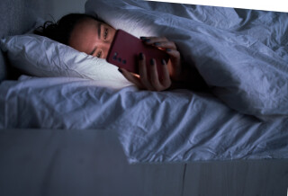 Mulher deitada na cama com o celular na mão