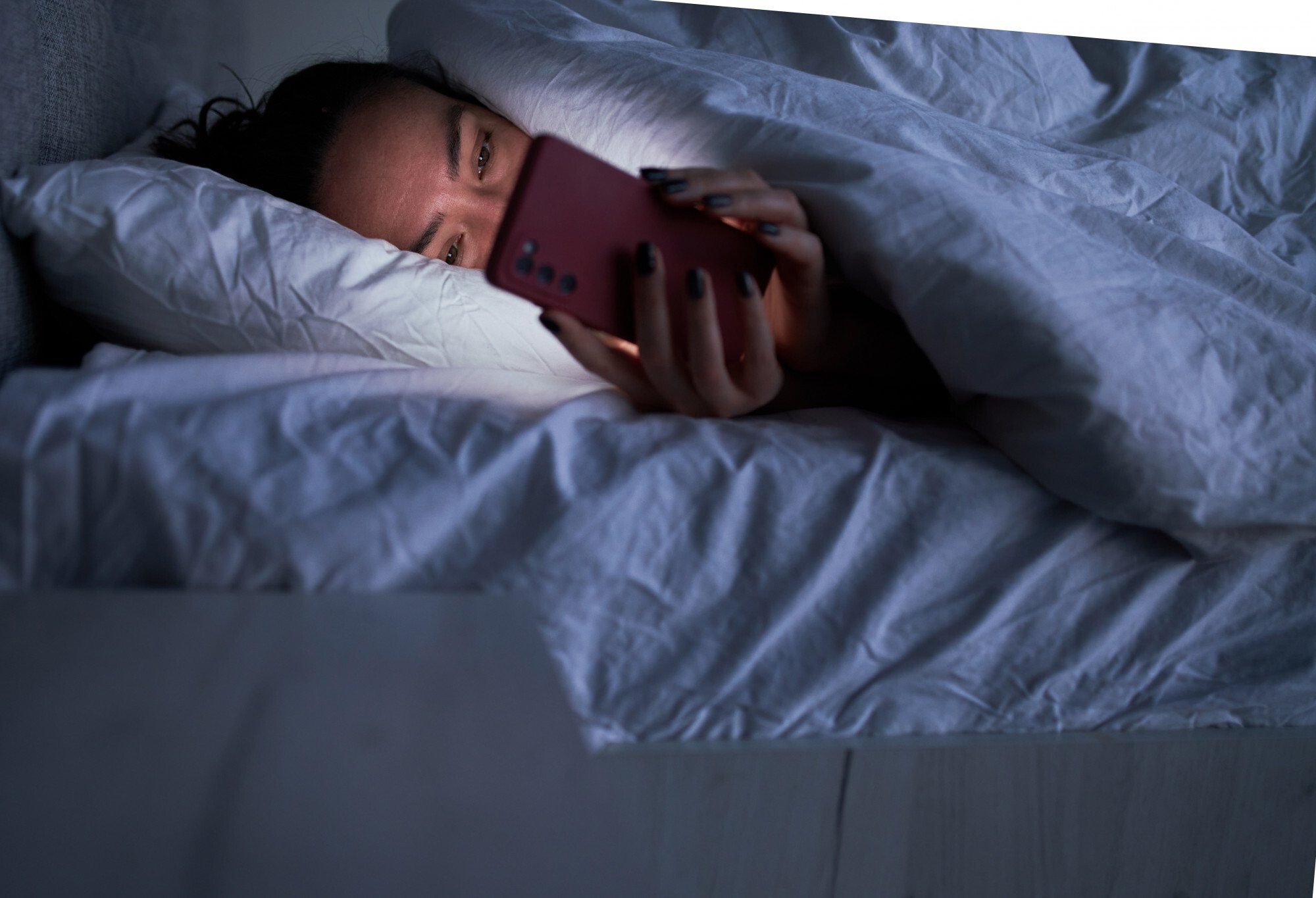 Mulher deitada na cama com o celular na mão
