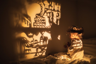 Criança sentada na cama com projetor criando imagens na parede