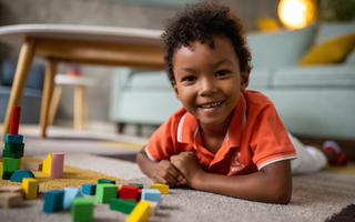 Menino deitado no tapete, sorridente, ao lado de peças construir