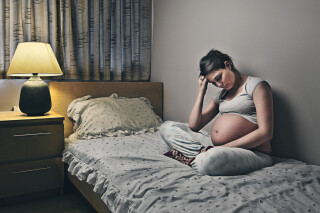 Mulher grávida com ansiedade sentada de pernas cruzadas em cima de cama