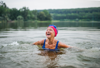 Mulher idosa sorrindo enquanto pratica natação em lago