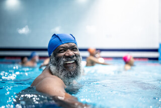 Homem idoso, de pele negra e barbas compridas e grisalhas, faz hidroginástica em uma piscina e usa uma touca de natação azul.