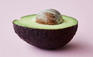 Abacate cortado ao meio em um fundo rosa