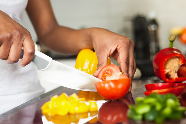 Mulher cortando legumes e frutas em bancada na cozinha