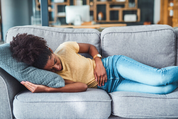 Na imagem, uma mulher negra está deitada em um sofá, com a mão no estômago