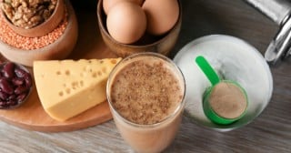 Queijo, ovos, copo com leite e scoop de whey protein em cima de uma mesa