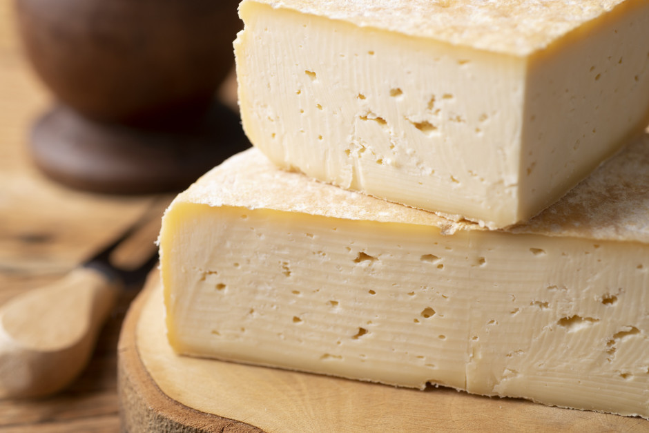 Foto aproximada de queijo canastra cortado ao meio, sobre uma tábua de madeira