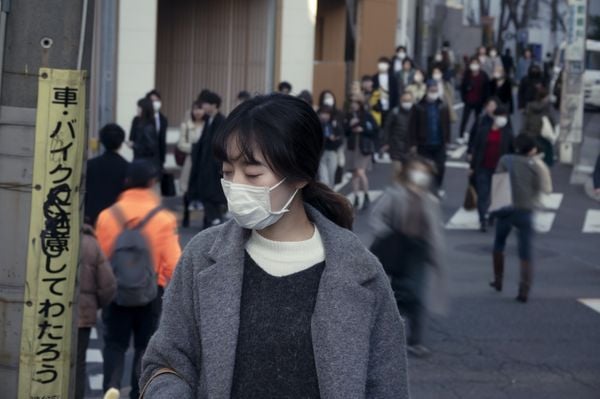 mulher japonesa andando na rua usando máscara. atrás dela, muitas pessoas também andam pela rua usando máscaras