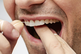 Close na boca de homem usando fio dental nos dentes