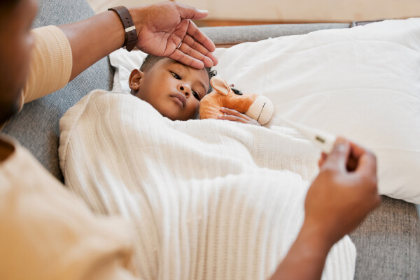 Criança doente, gripada e fria na cama, triste e doente com alergia e mal em casa com sua mãe preocupada, enquanto coloca uma mão em sua testa e olha o termômetro com a outra