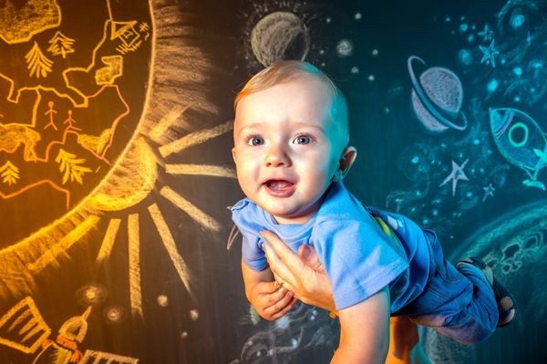 Bebê em frente a lousa com desenhos do sistema solar