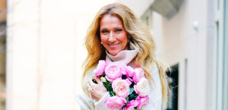 Céline Dion, de cabelos soltos, vestindo blusa branca e segurando um buquê de flores rosas