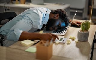 Homem cochilando em frente ao notebook do trabalho