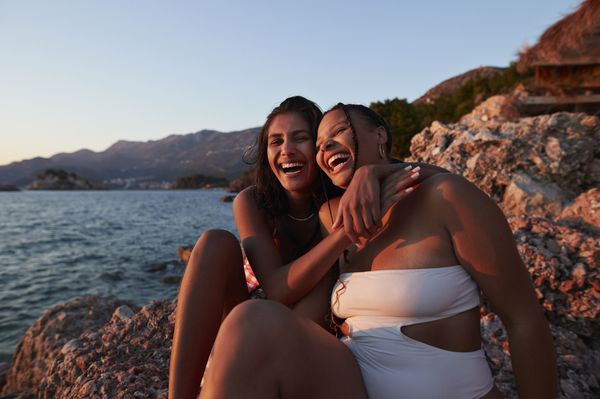 duas mulheres amigas sentadas na praia se abraçando
