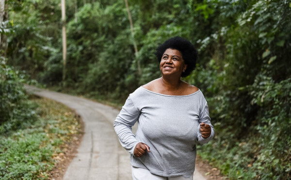 Mulher de blusa cinza correndo em uma trilha enquanto olha para cima sorrindo