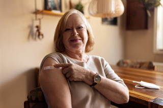 Mulher idosa sentada apontando para curativo de vacina em seu braço
