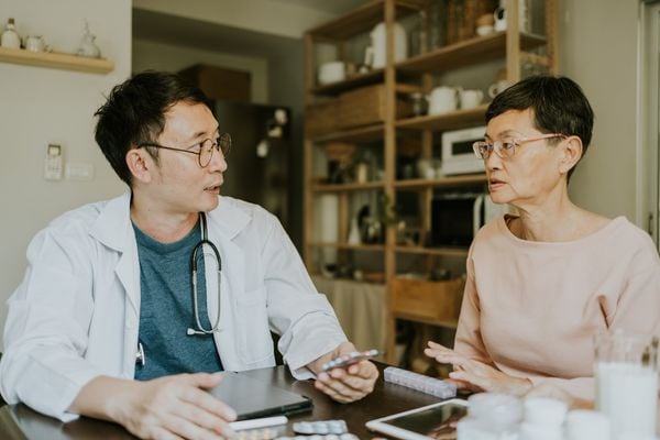 médico homem asiático usando jaleco sentado ao lado de uma mulher paciente asiática de meia idade enquanto receita remédios