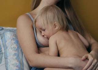 Criança sentada no colo da mãe enquanto é amamentada