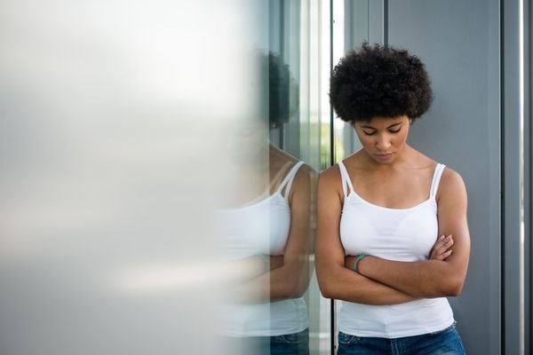 Mulher com a cabeça baixa, braços cruzados e feição triste