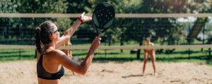 Mulher jogando beach tennis em quadra de areia com outras pessoas