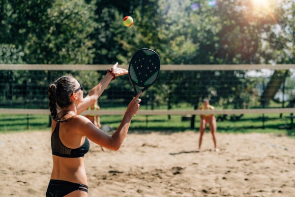 Mulher jogando beach tennis em quadra de areia com outras pessoas