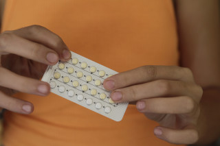 Mulher de blusa laranja segurando cartela de anticoncepcionais
