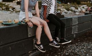 Close up de um casal hétero sentado em um muro. O recorte da imagem não mostra suas cabeças