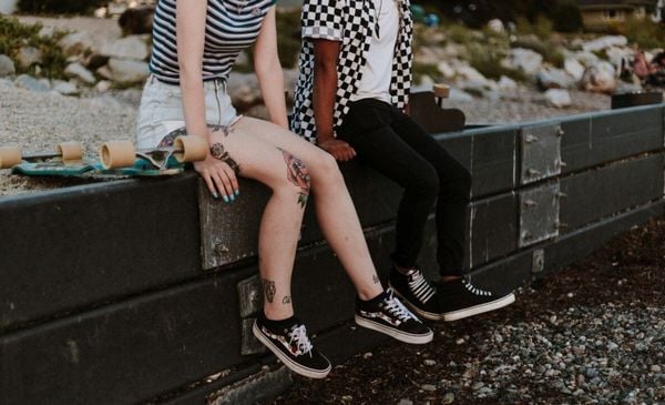 Close up de um casal hétero sentado em um muro. O recorte da imagem não mostra suas cabeças