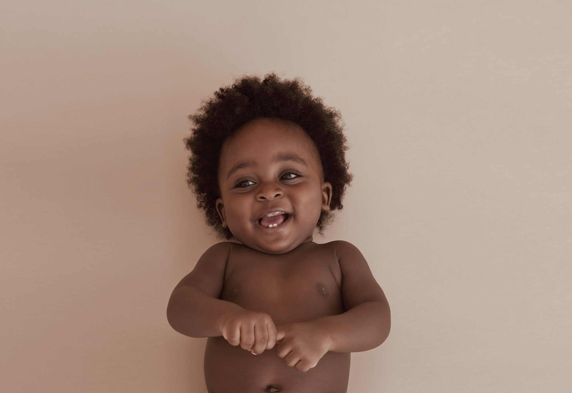 bebê sorrindo deitado em um fundo rosa