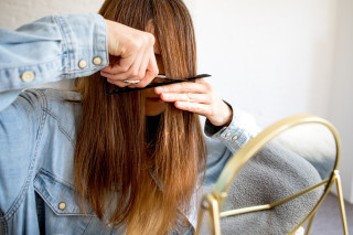 Mulher na frente de espelho cortando o cabelo sozinha com tesoura